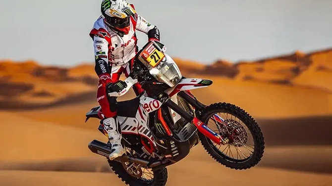 Motorcycle rider, male on full gear, performing tricks on the desert